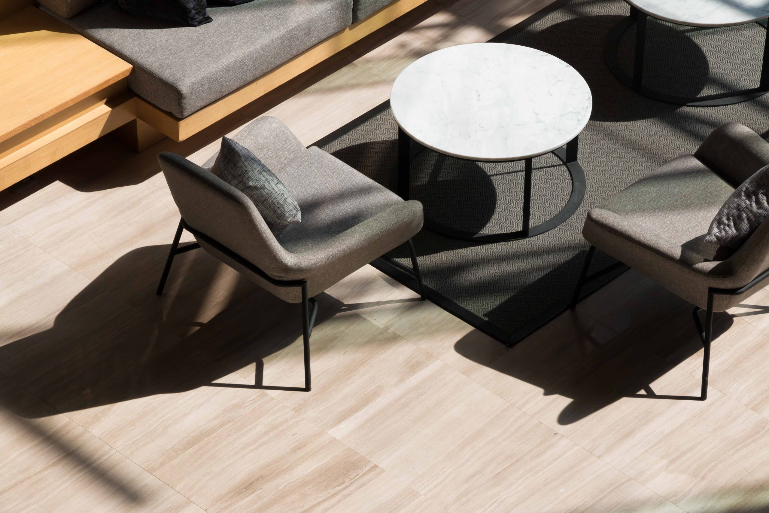 Vue de dessus du salon du lobby avec canapé long, fauteuils, tables rondes et moquette grise sur sol en marbre dans un hôtel moderne.